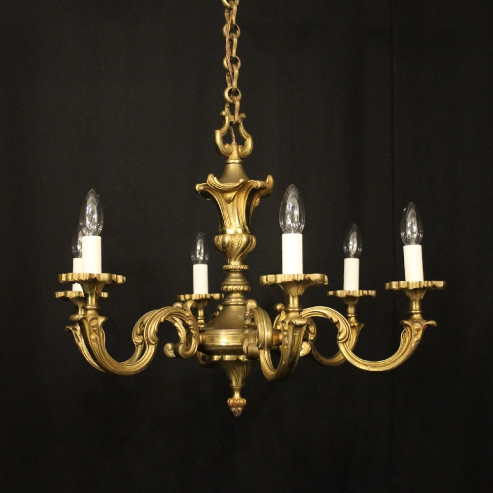 A six-arm French gilt bronze chandelier featuring scrolled arms, leaf motifs, and faux candle bulb holders hanging from a central column.