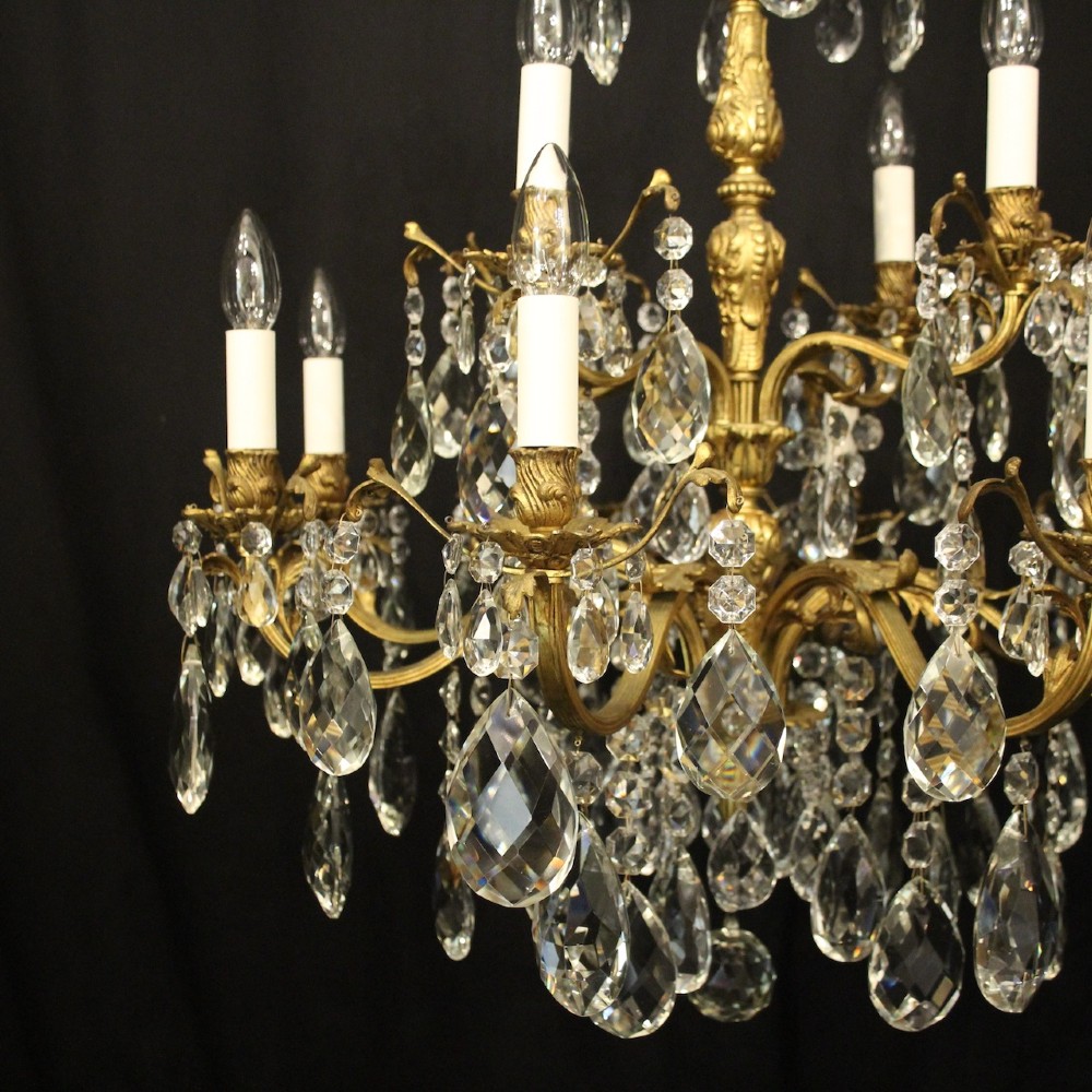 A French gilded bronze twelve-light chandelier featuring curved scrolling arms, cream candle-style light holders, and cascading faceted crystal drops. View II