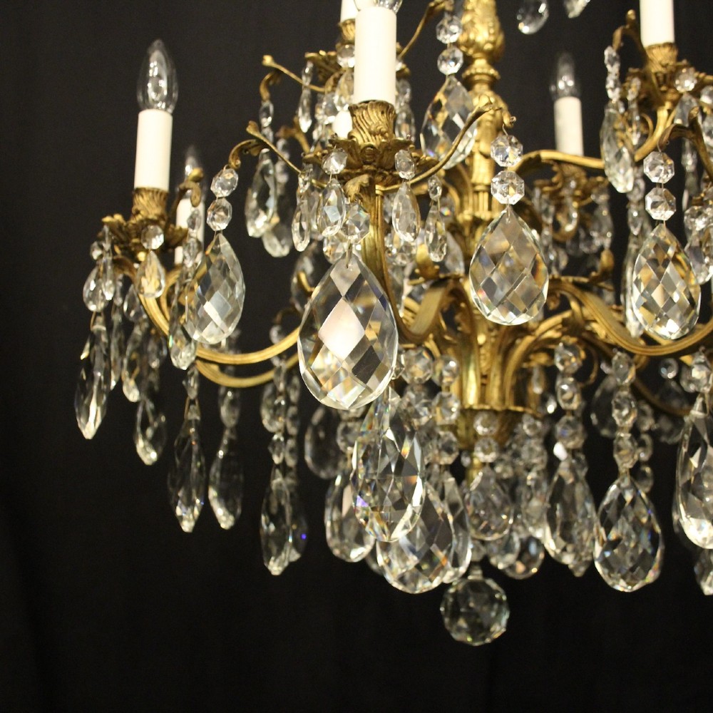 A French gilded bronze twelve-light chandelier featuring curved scrolling arms, cream candle-style light holders, and cascading faceted crystal drops. View III