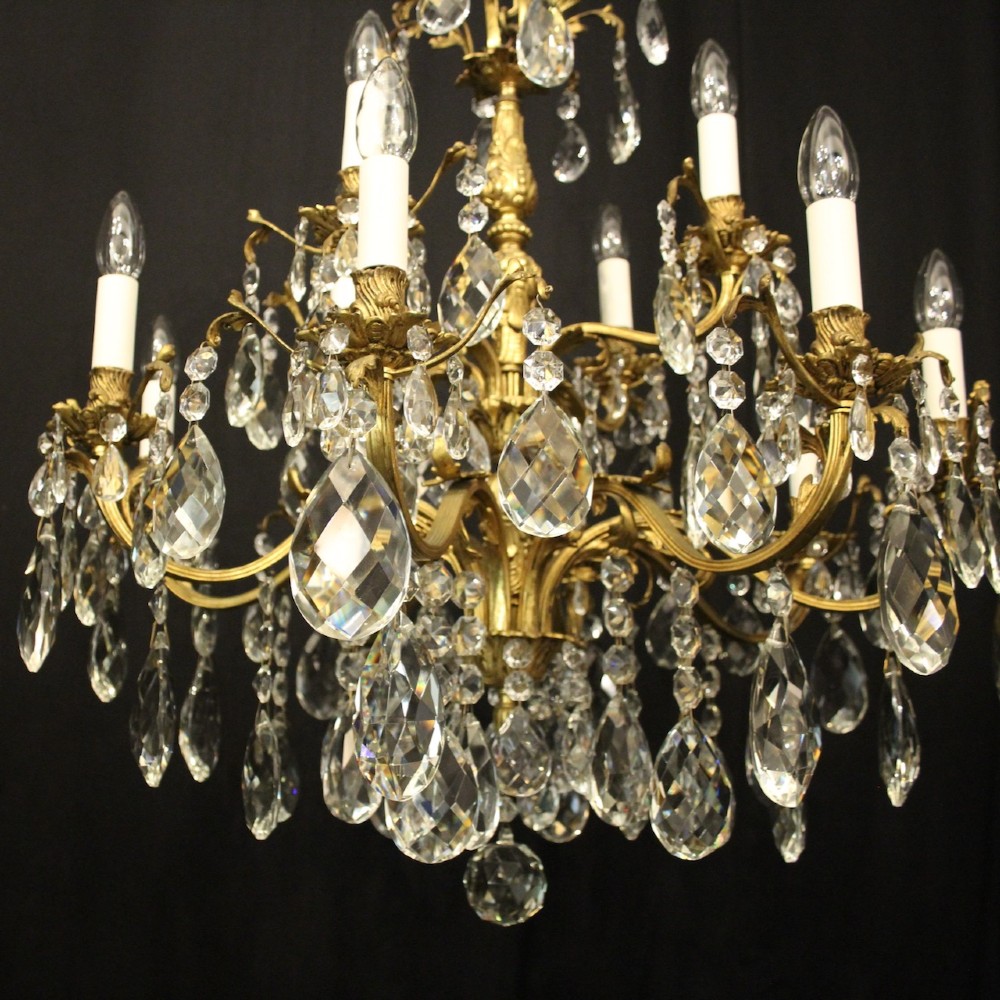 A French gilded bronze twelve-light chandelier featuring curved scrolling arms, cream candle-style light holders, and cascading faceted crystal drops. View IV
