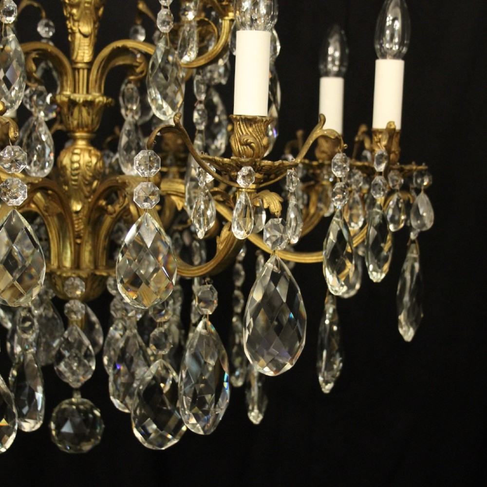 A French gilded bronze twelve-light chandelier featuring curved scrolling arms, cream candle-style light holders, and cascading faceted crystal drops. View V