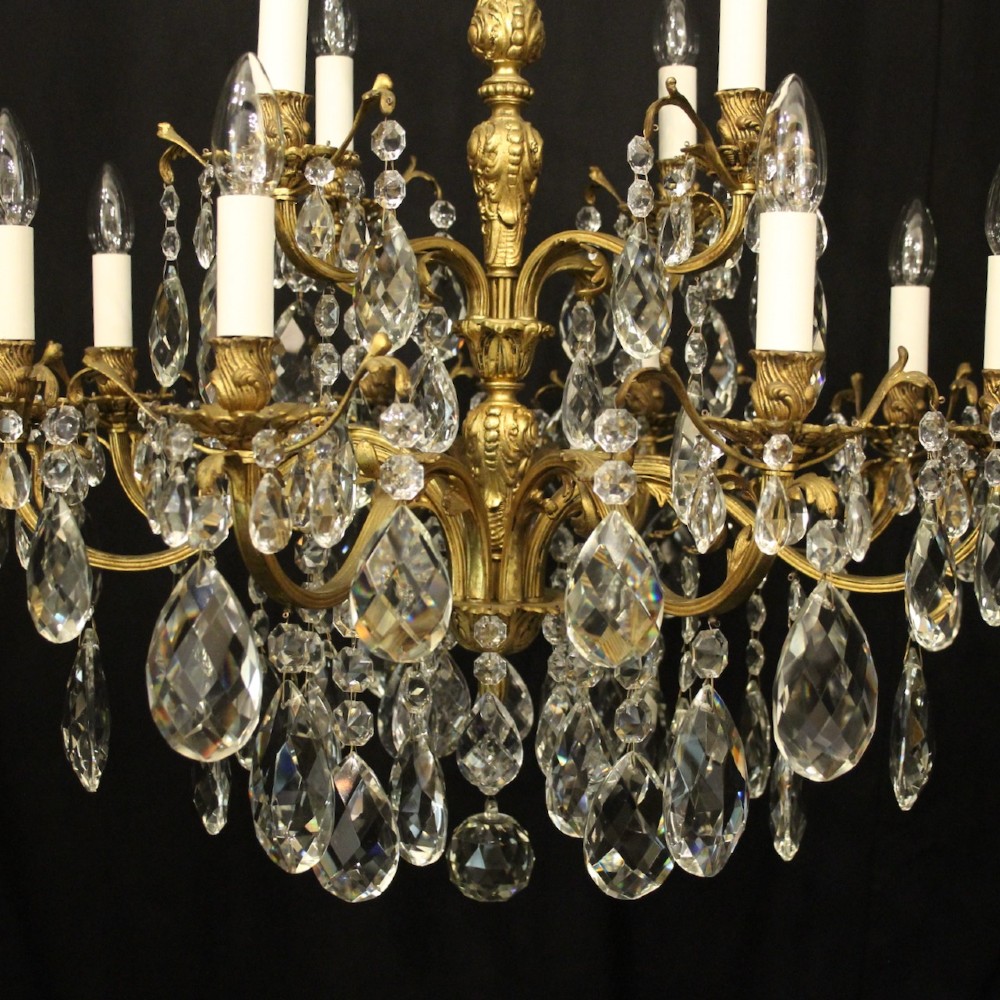 A French gilded bronze twelve-light chandelier featuring curved scrolling arms, cream candle-style light holders, and cascading faceted crystal drops. View VII