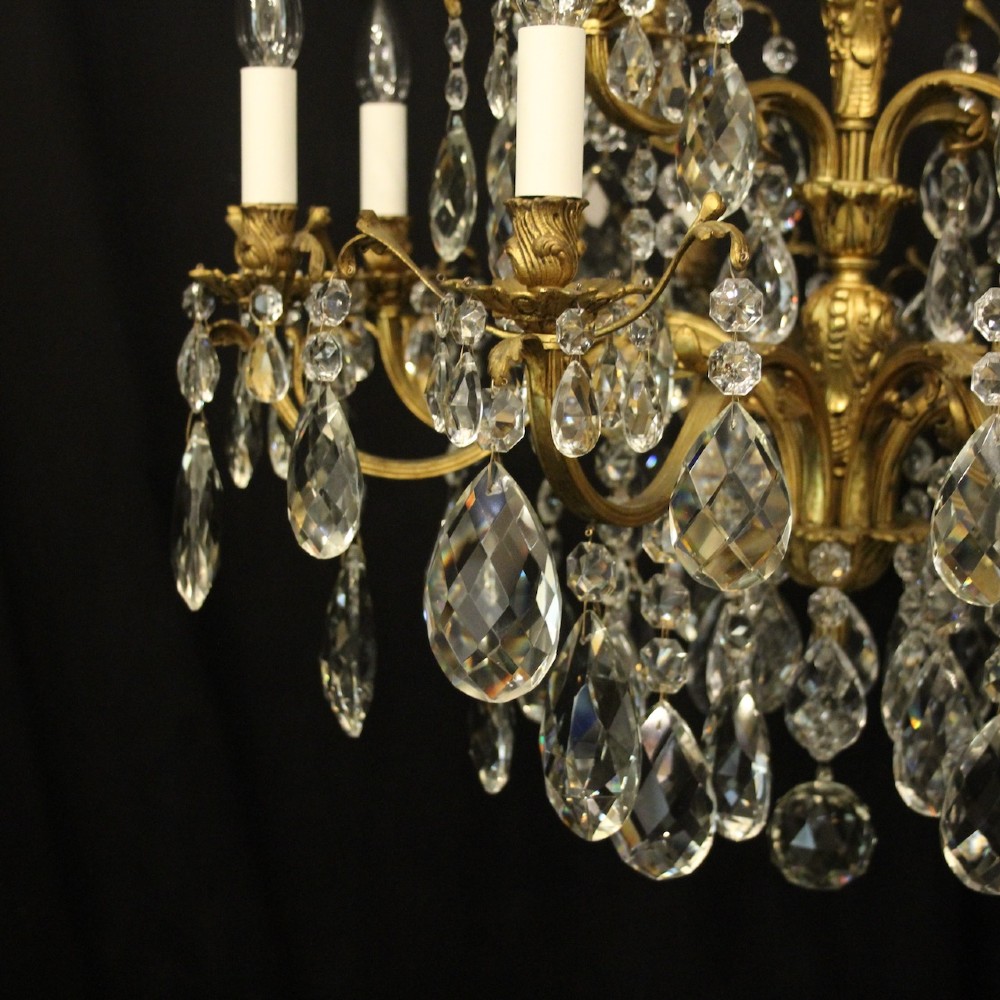 A French gilded bronze twelve-light chandelier featuring curved scrolling arms, cream candle-style light holders, and cascading faceted crystal drops. View VIII