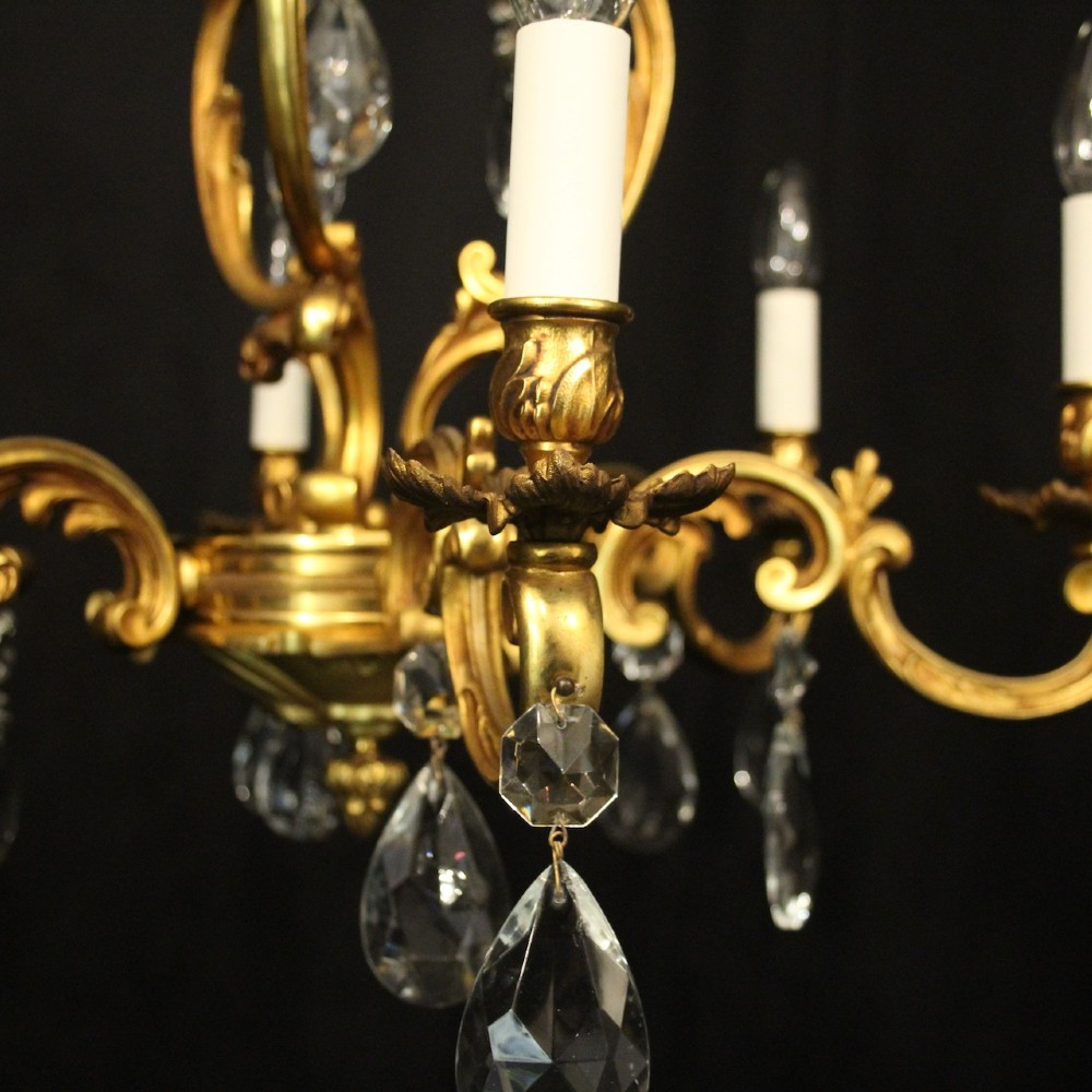 A French gilt bronze six-light chandelier decorated with scrolling arms and suspended cut crystal teardrop pendants. View V