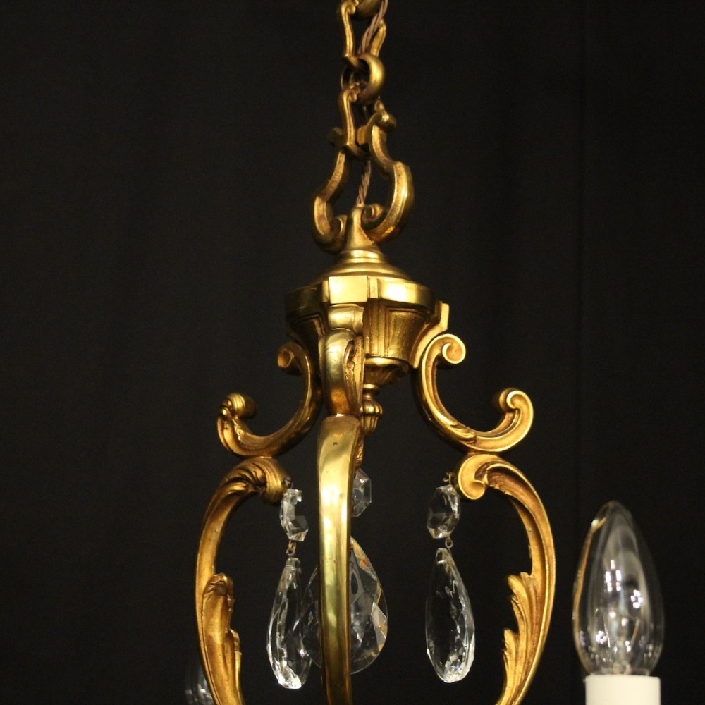 A French gilt bronze six-light chandelier decorated with scrolling arms and suspended cut crystal teardrop pendants. View IX