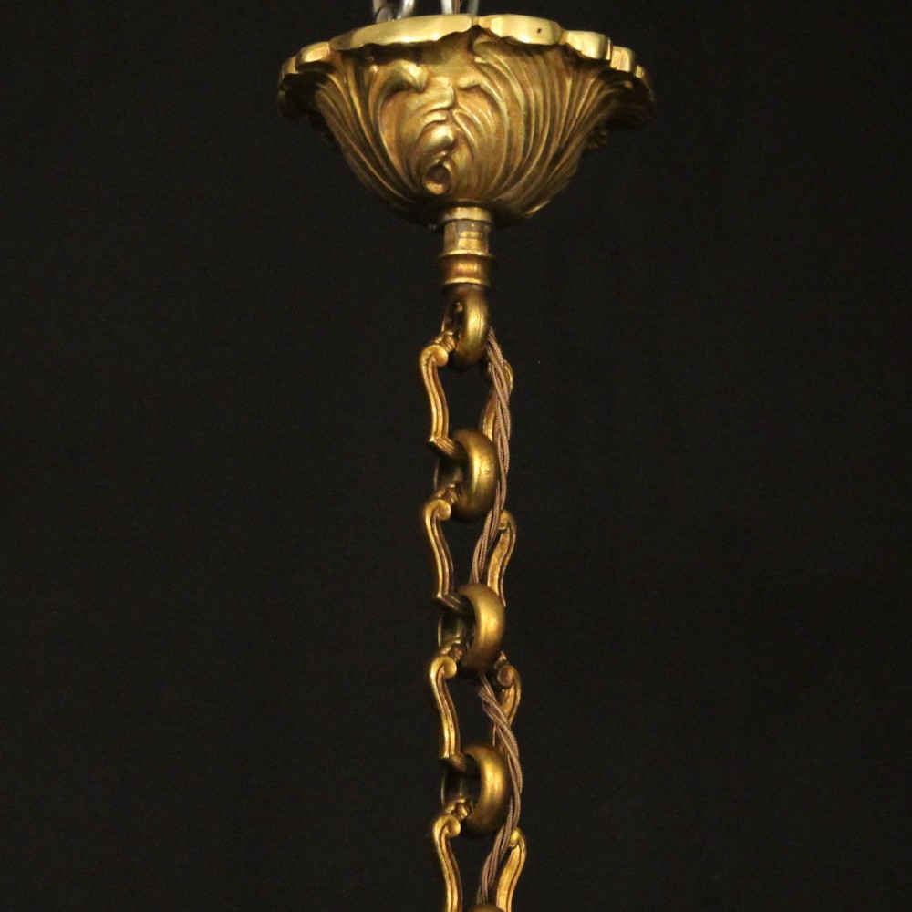 A French gilt bronze six-light chandelier decorated with scrolling arms and suspended cut crystal teardrop pendants. View X