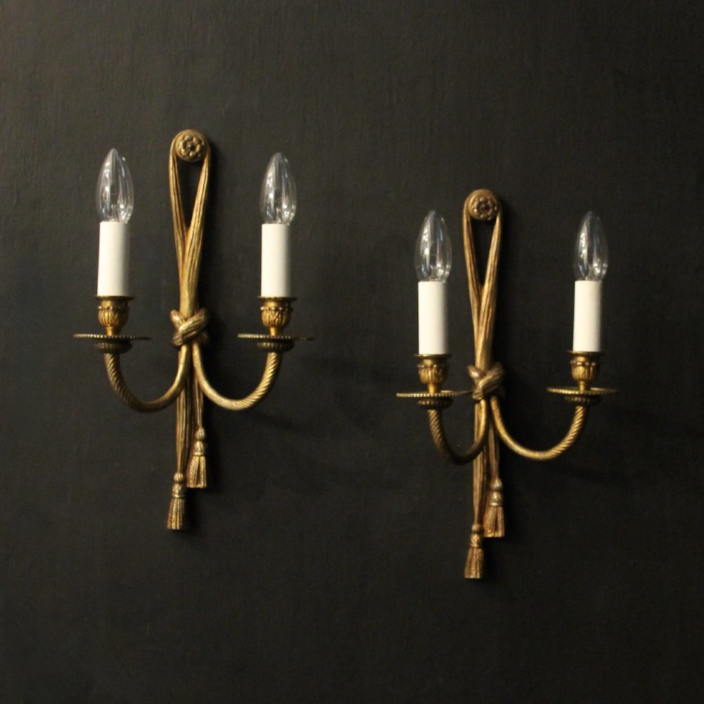 A pair of French gilded brass twin-arm wall sconces featuring a tied rope and tassel motif with candle-style bulb fittings.