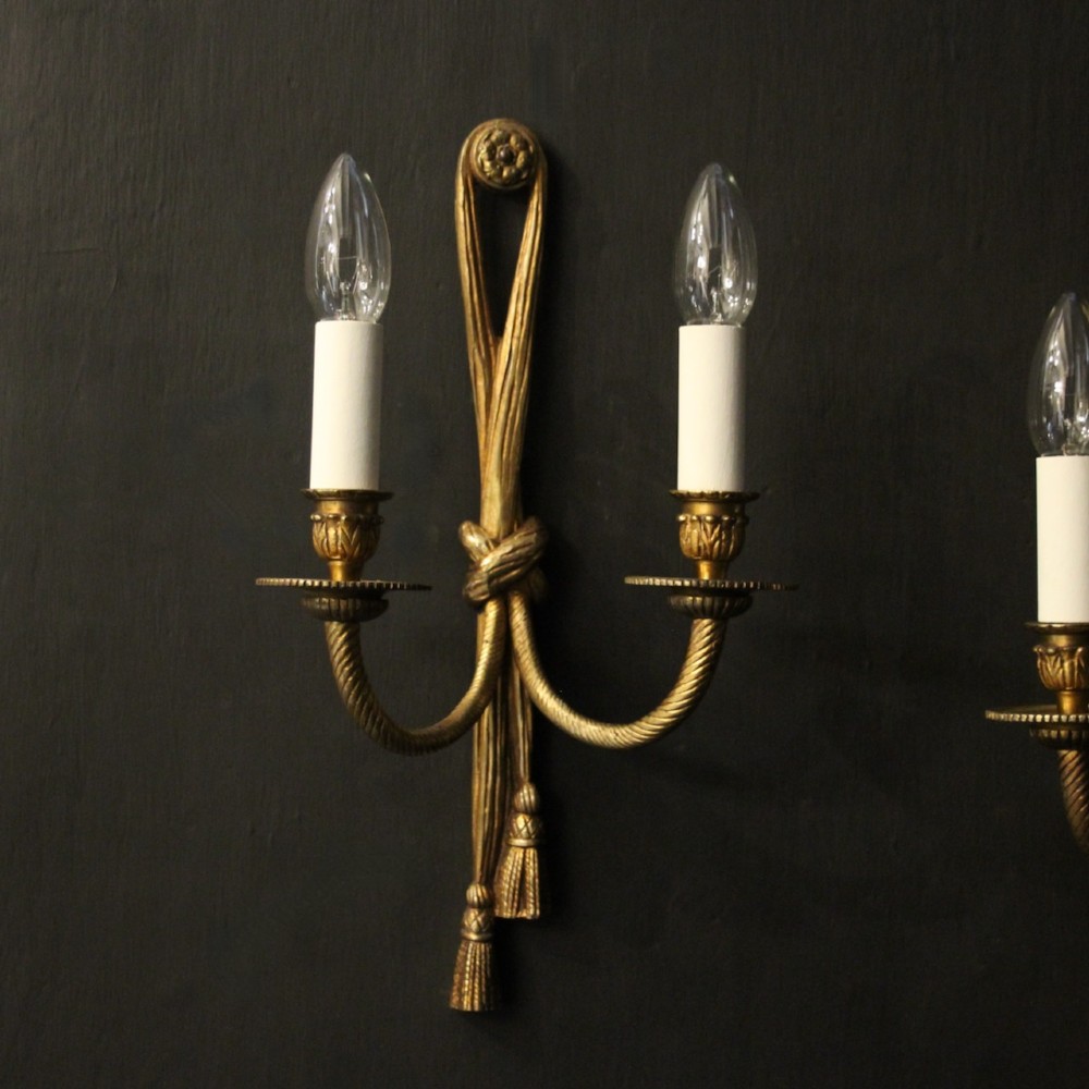 A pair of French gilded brass twin-arm wall sconces featuring a tied rope and tassel motif with candle-style bulb fittings. View II