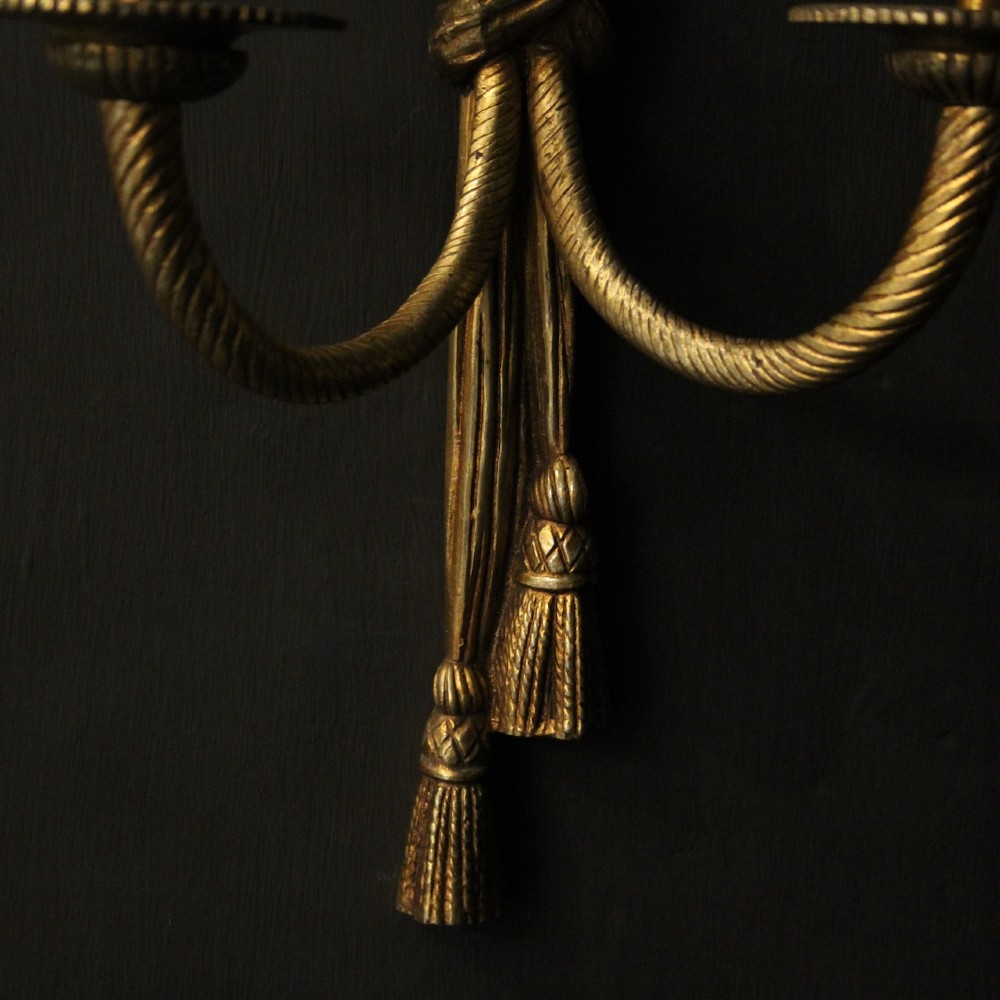 A pair of French gilded brass twin-arm wall sconces featuring a tied rope and tassel motif with candle-style bulb fittings. View IX