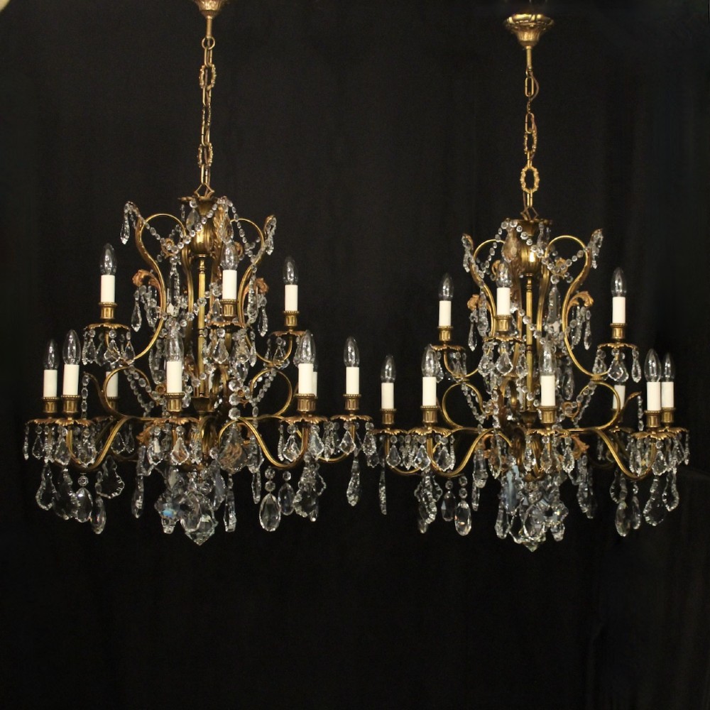 A pair of twelve-light French chandeliers made from gilt metal frames heavily decorated with hanging faceted crystal drops and candleshaft bulb holders.