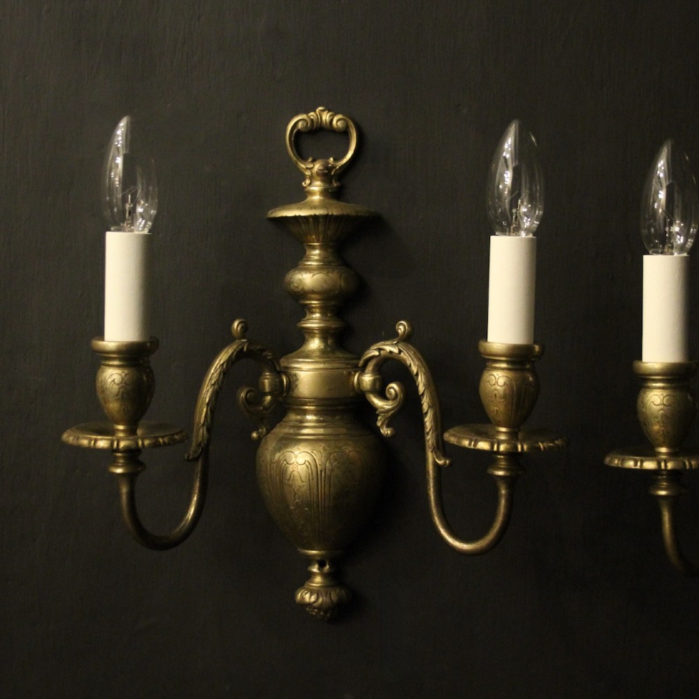 A pair of antique bronze twin-arm wall lights with urn-shaped central bodies and decorative scroll arms against a dark backdrop. View II