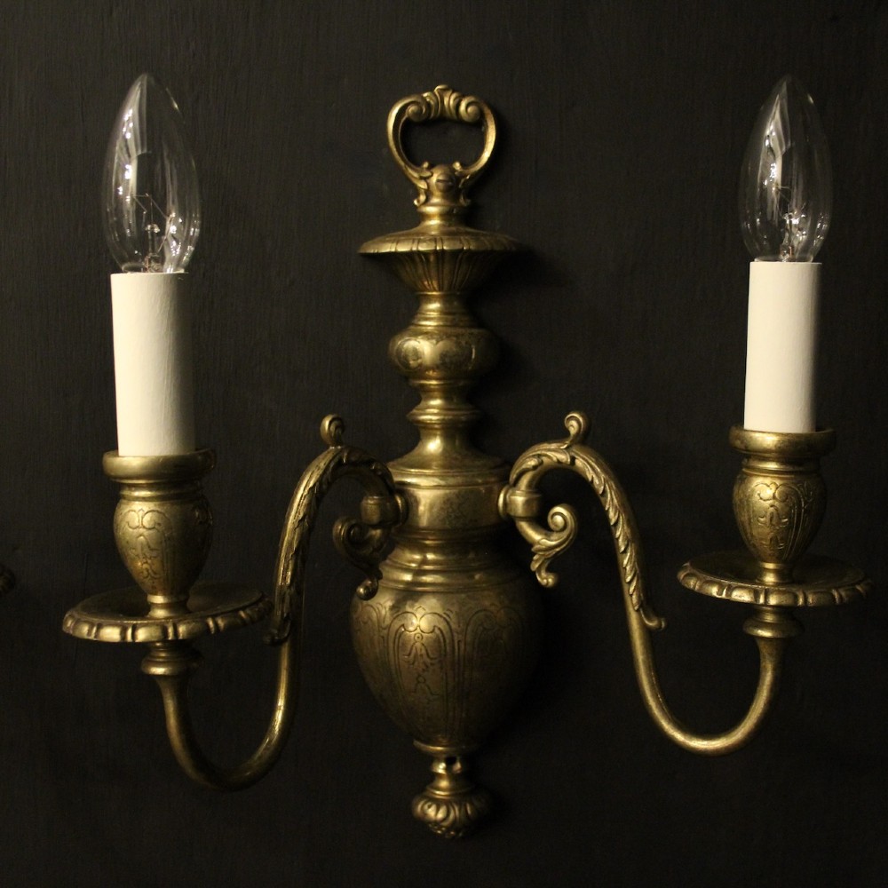 A pair of antique bronze twin-arm wall lights with urn-shaped central bodies and decorative scroll arms against a dark backdrop. View III