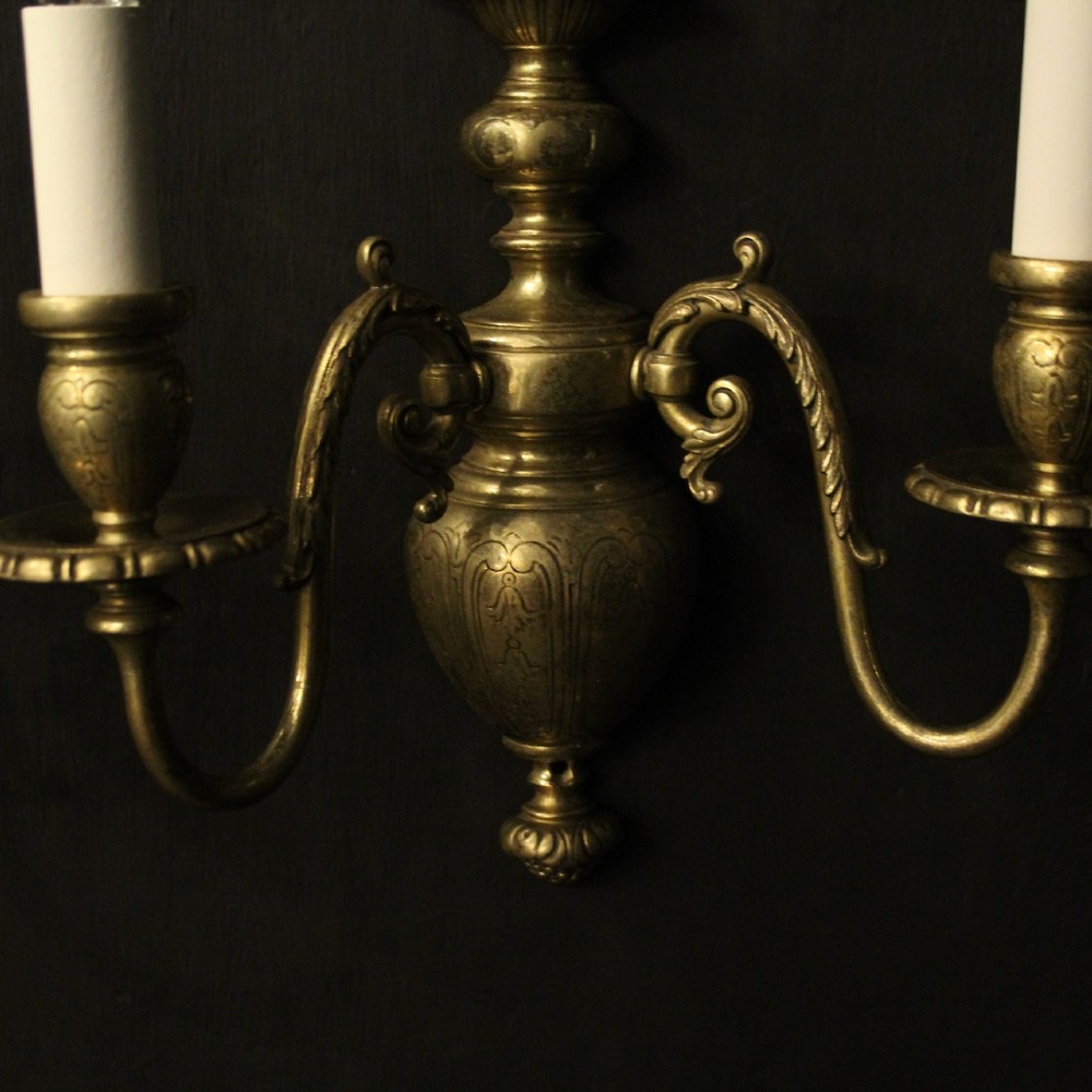 A pair of antique bronze twin-arm wall lights with urn-shaped central bodies and decorative scroll arms against a dark backdrop. View IV