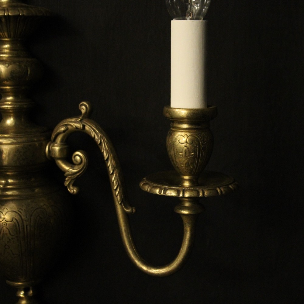 A pair of antique bronze twin-arm wall lights with urn-shaped central bodies and decorative scroll arms against a dark backdrop. View V