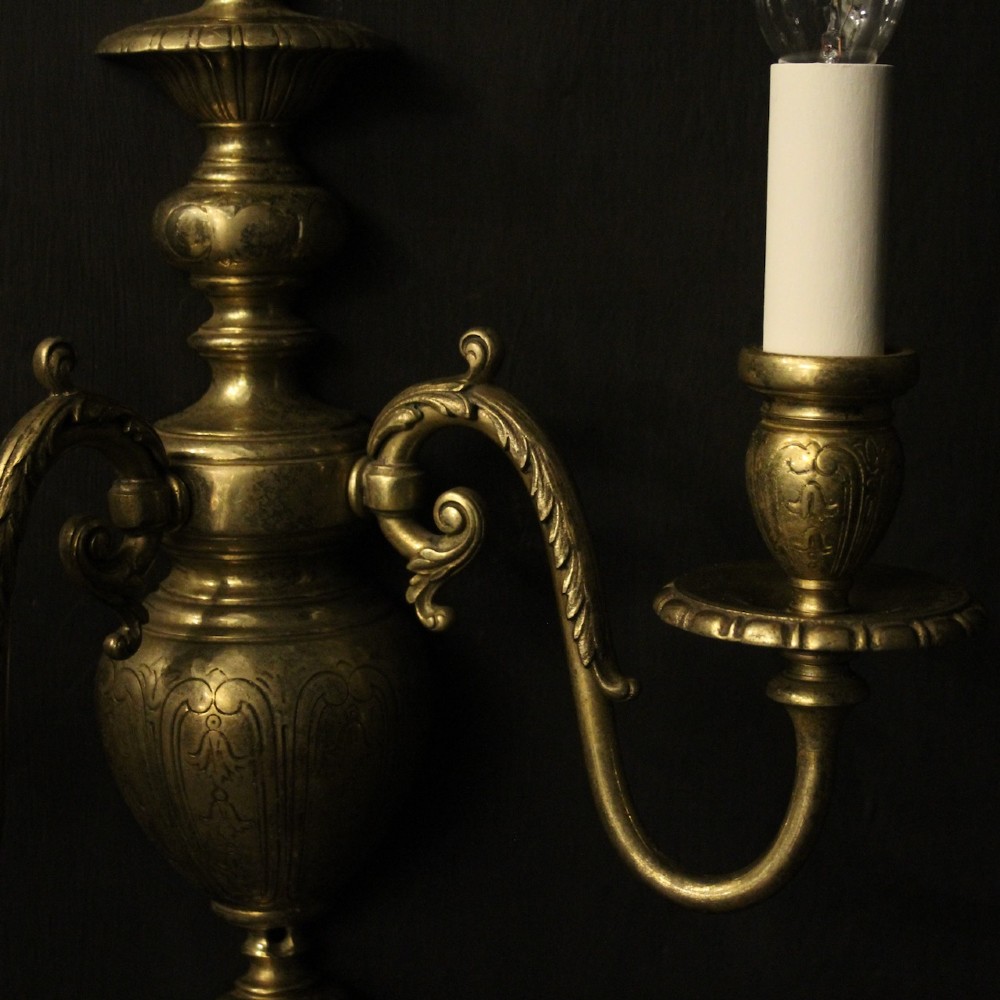 A pair of antique bronze twin-arm wall lights with urn-shaped central bodies and decorative scroll arms against a dark backdrop. View VI