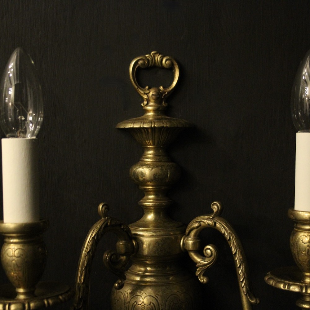 A pair of antique bronze twin-arm wall lights with urn-shaped central bodies and decorative scroll arms against a dark backdrop. View VIII