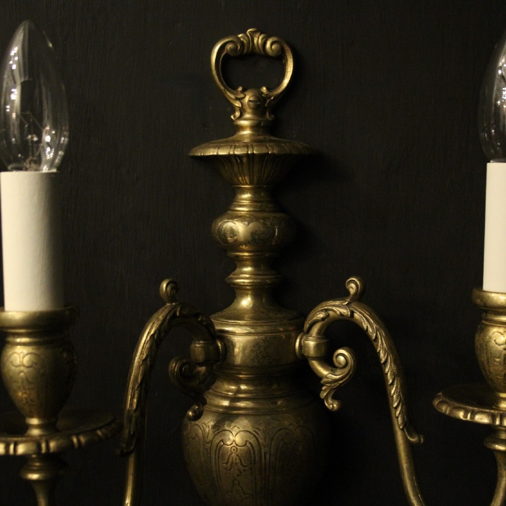 A pair of antique bronze twin-arm wall lights with urn-shaped central bodies and decorative scroll arms against a dark backdrop. View IX