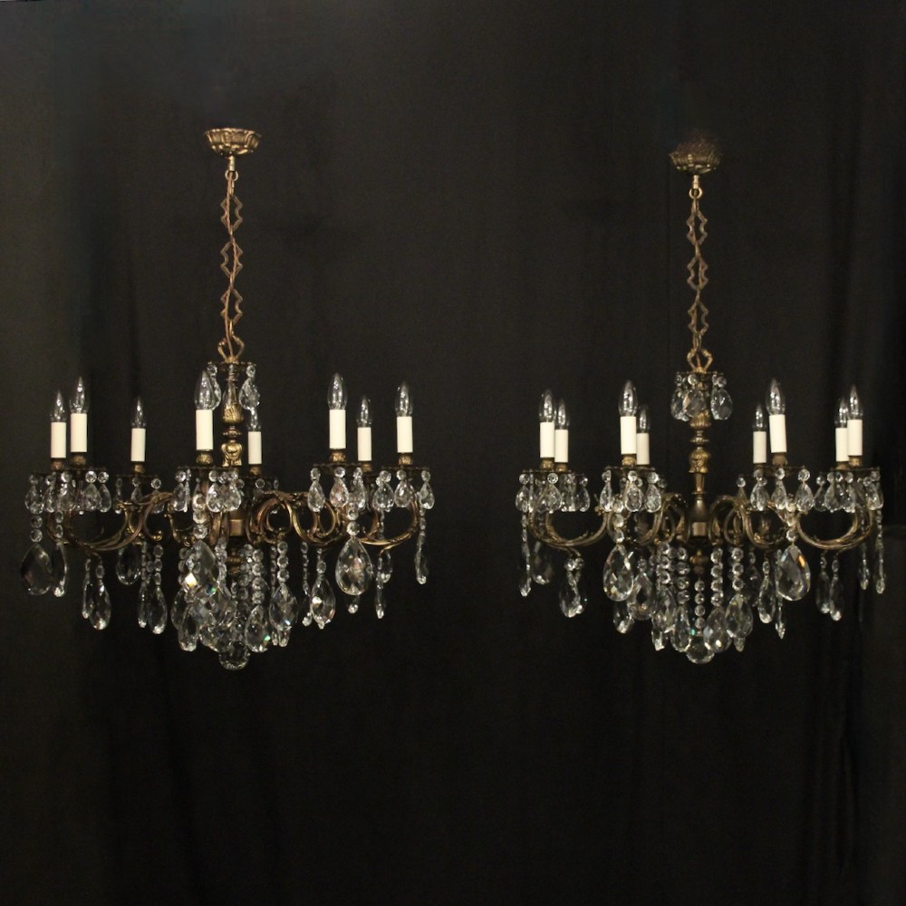 A pair of antique French eight-light brass chandeliers featuring scrolled arms and cut crystal teardrop prisms.