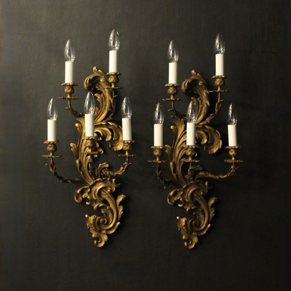 A pair of ornate French Rococo style gilded bronze five-arm wall sconces featuring acanthus leaf scrollwork.