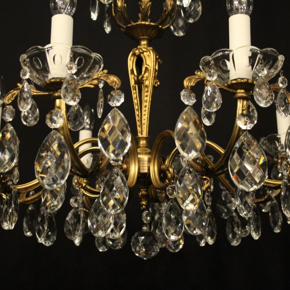 An eight-arm French chandelier featuring a gilded brass frame decorated with hanging cut-crystal glass drops and white candle-style bulb holders. View V