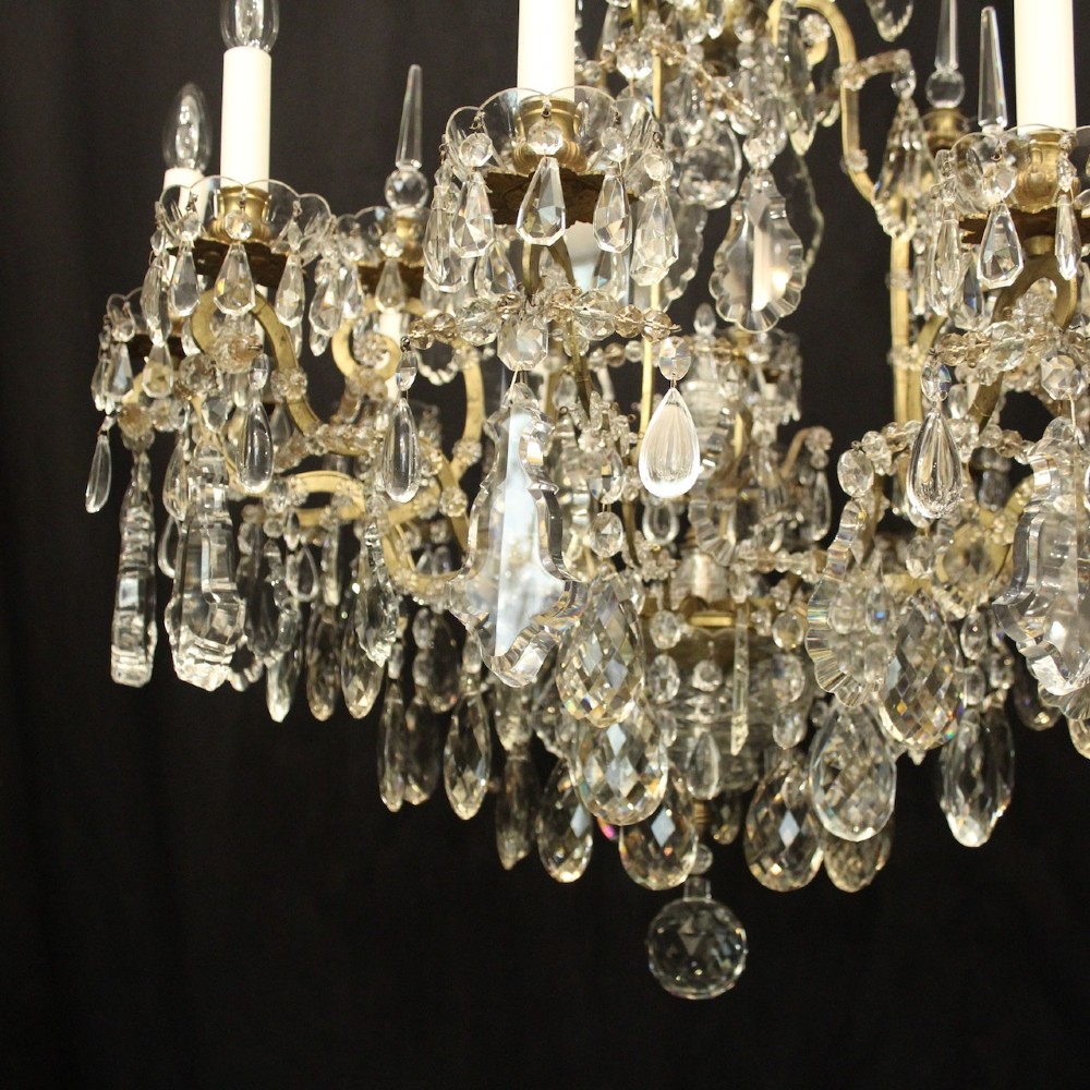 A large French antique twelve-light chandelier featuring a gilded frame dressed with cut crystal teardrop pendants and central glass pinnacles. View VI