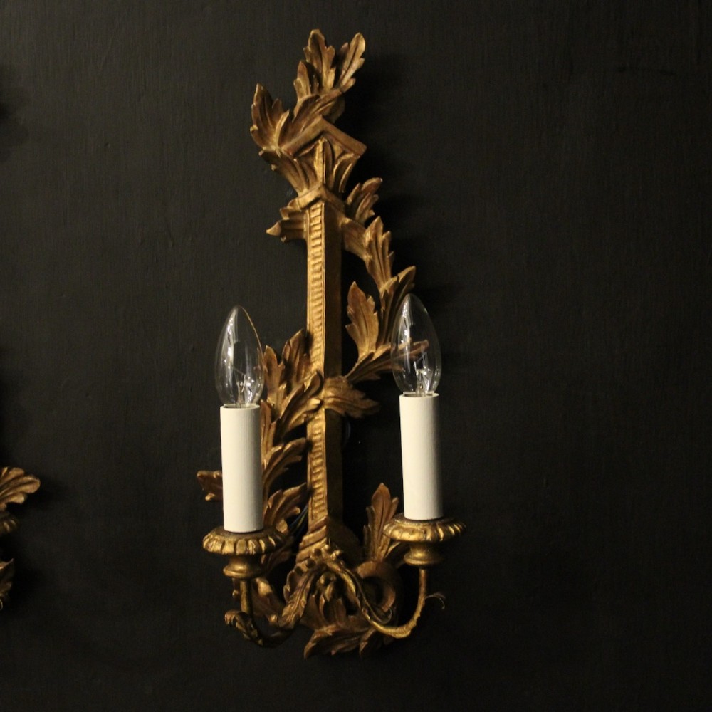 A pair of French carved giltwood two-arm wall sconces featuring leaf ornamentation and white candle sleeves with clear light bulbs. View II