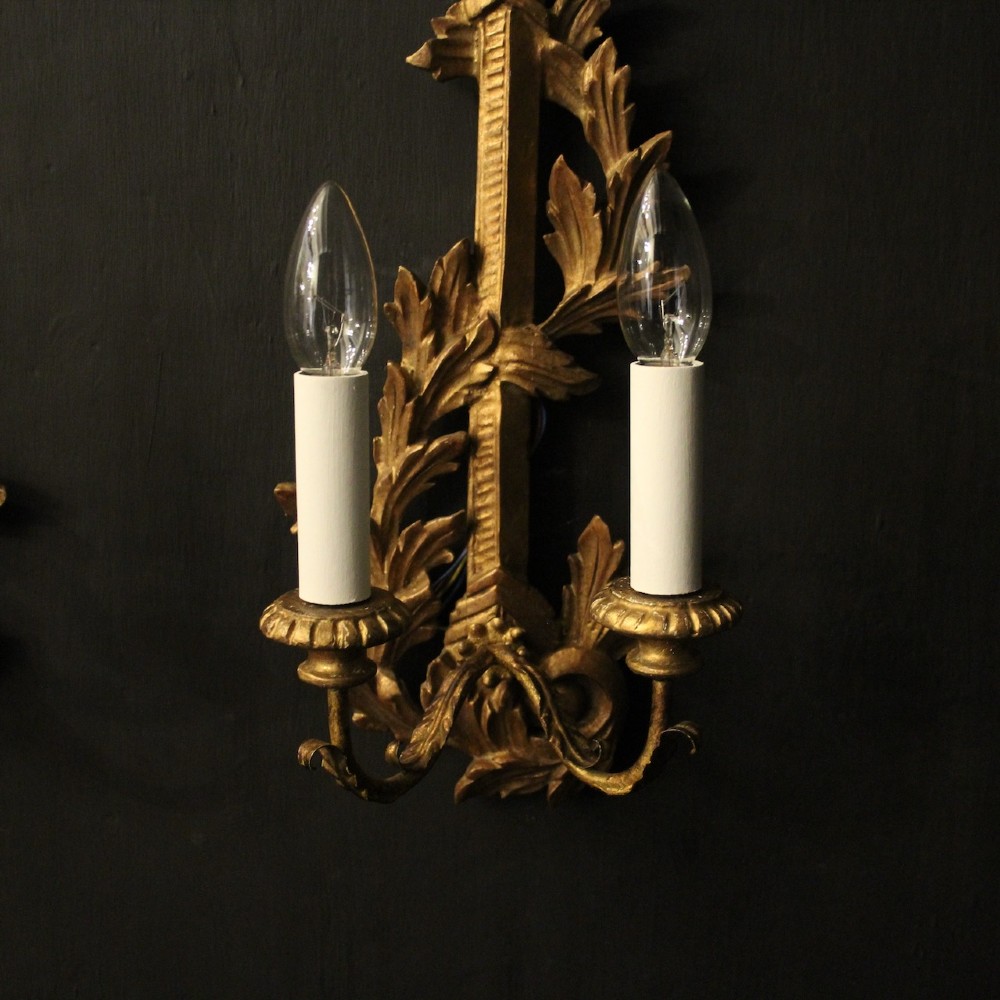 A pair of French carved giltwood two-arm wall sconces featuring leaf ornamentation and white candle sleeves with clear light bulbs. View III