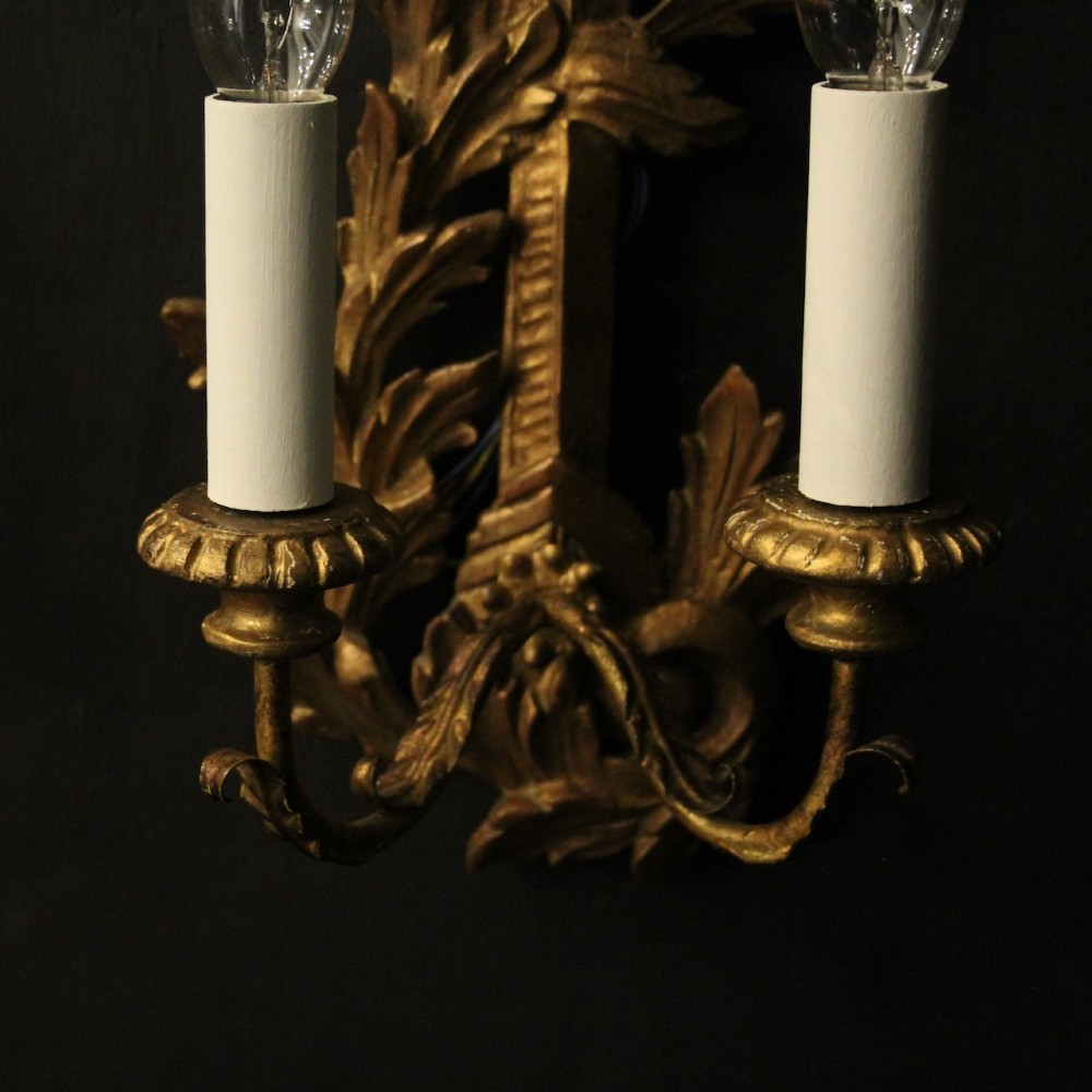 A pair of French carved giltwood two-arm wall sconces featuring leaf ornamentation and white candle sleeves with clear light bulbs. View IV