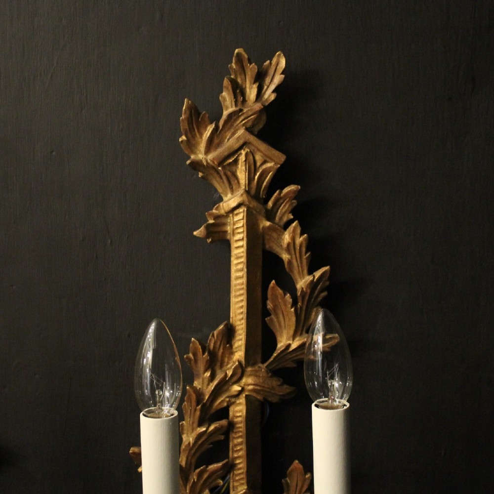 A pair of French carved giltwood two-arm wall sconces featuring leaf ornamentation and white candle sleeves with clear light bulbs. View V