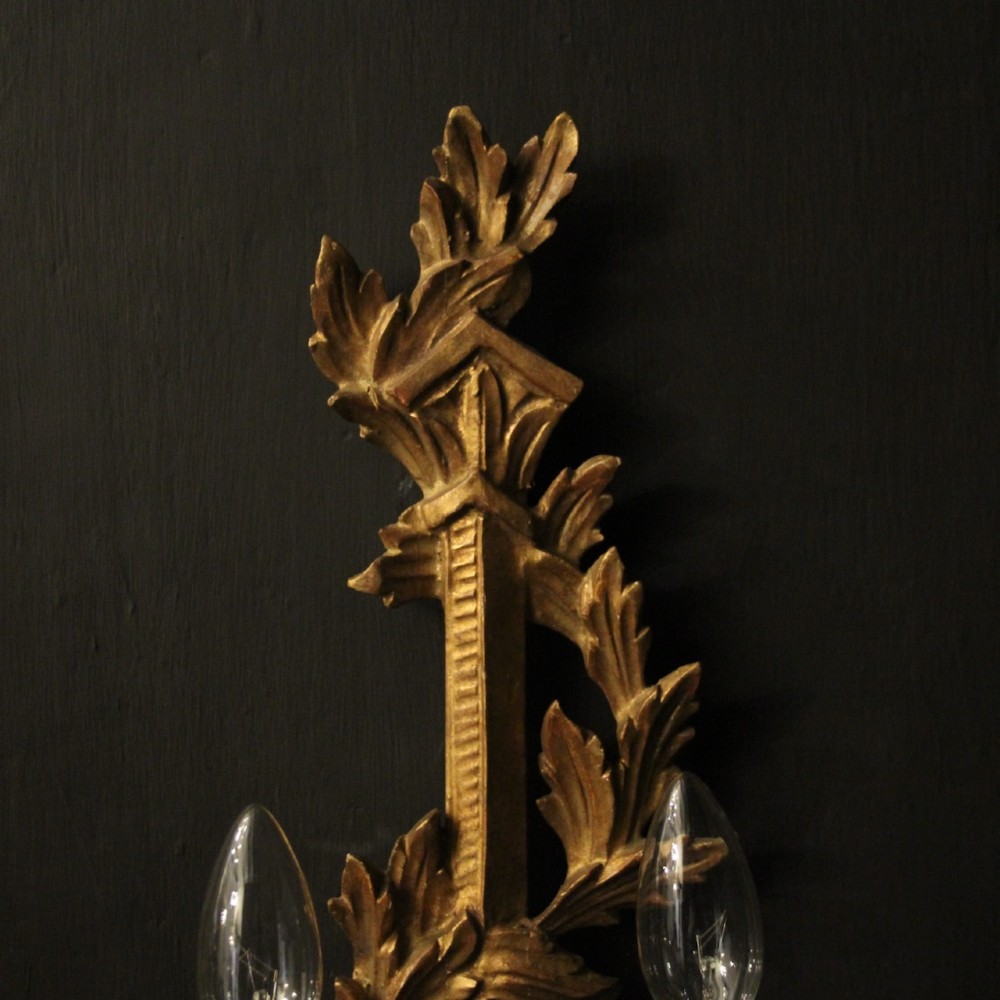 A pair of French carved giltwood two-arm wall sconces featuring leaf ornamentation and white candle sleeves with clear light bulbs. View VI