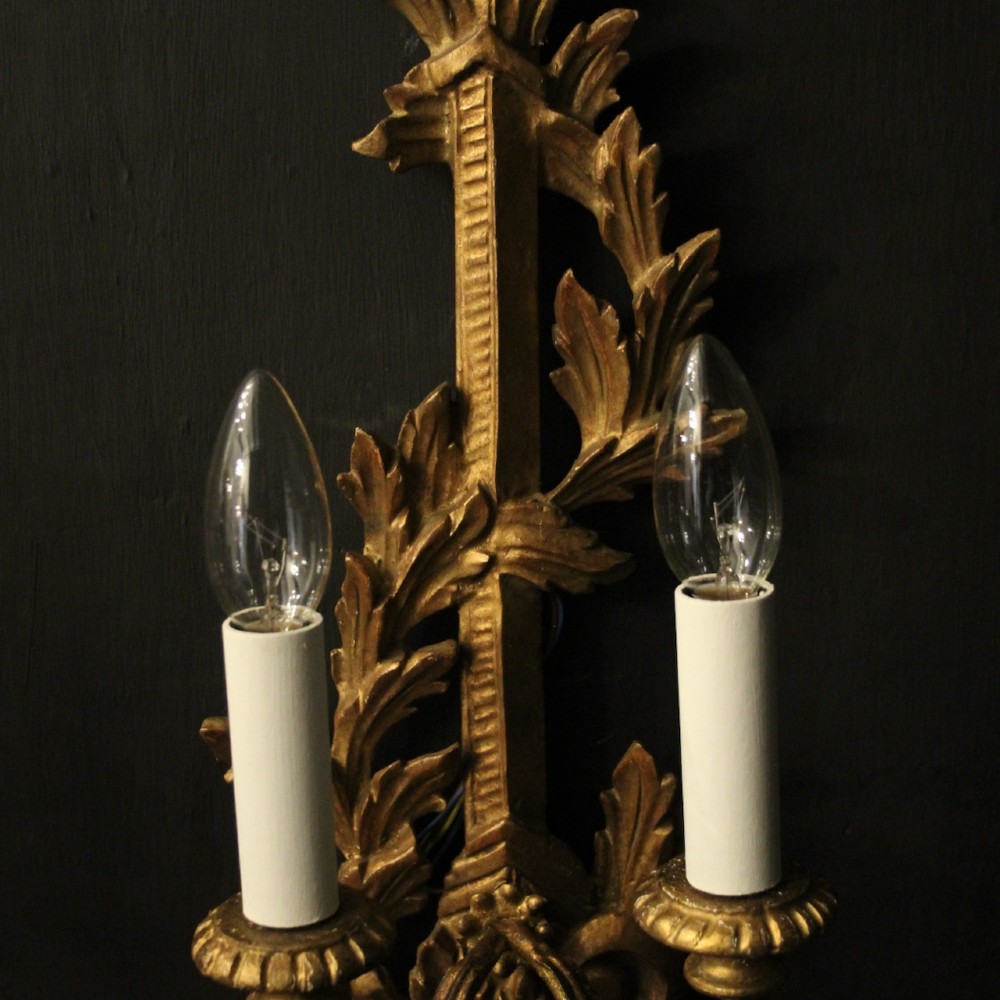 A pair of French carved giltwood two-arm wall sconces featuring leaf ornamentation and white candle sleeves with clear light bulbs. View VII