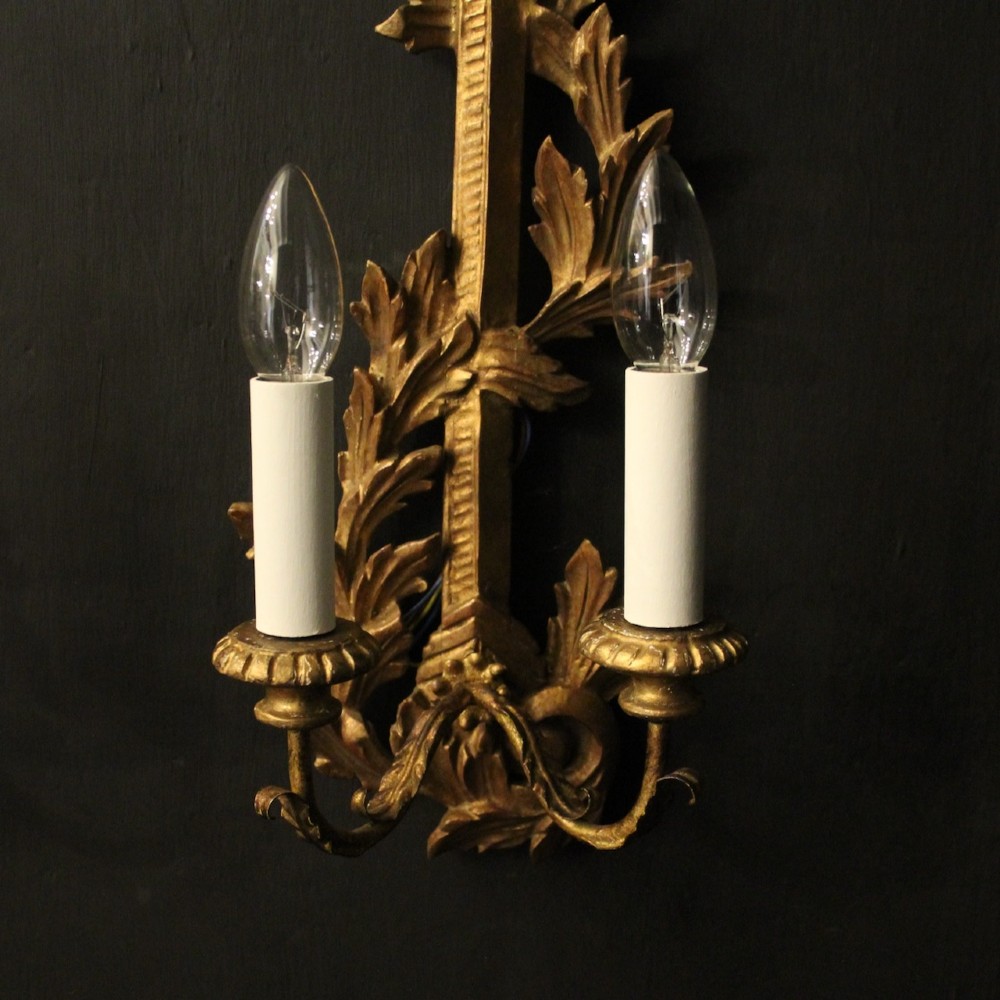 A pair of French carved giltwood two-arm wall sconces featuring leaf ornamentation and white candle sleeves with clear light bulbs. View VIII