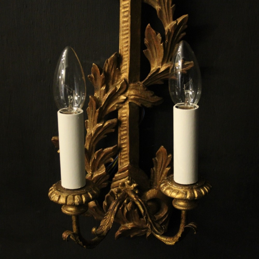 A pair of French carved giltwood two-arm wall sconces featuring leaf ornamentation and white candle sleeves with clear light bulbs. View IX