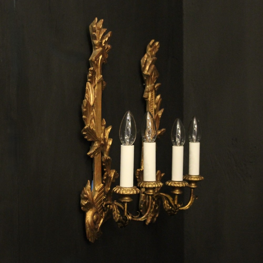 A pair of French carved giltwood two-arm wall sconces featuring leaf ornamentation and white candle sleeves with clear light bulbs. View X