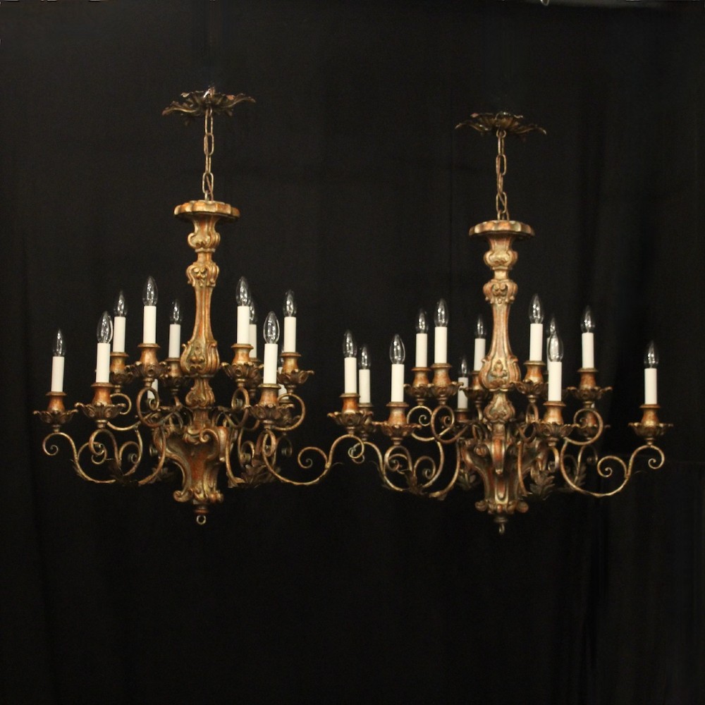 A pair of twelve-light Italian Florentine chandeliers featuring carved gilt wood scrollwork, polychrome painted details, and candle-style bulb holders.