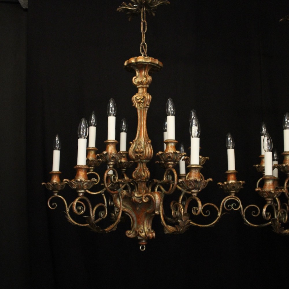 A pair of twelve-light Italian Florentine chandeliers featuring carved gilt wood scrollwork, polychrome painted details, and candle-style bulb holders. View II
