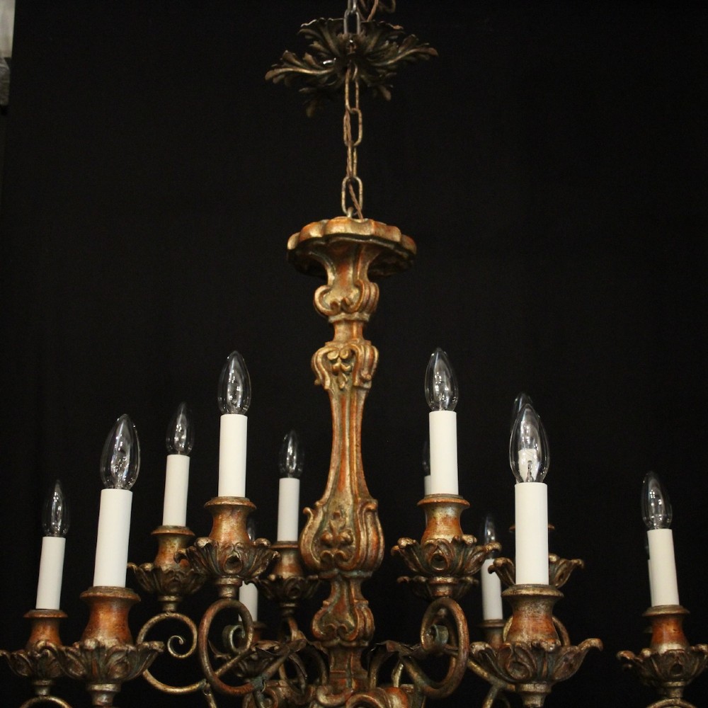 A pair of twelve-light Italian Florentine chandeliers featuring carved gilt wood scrollwork, polychrome painted details, and candle-style bulb holders. View IV