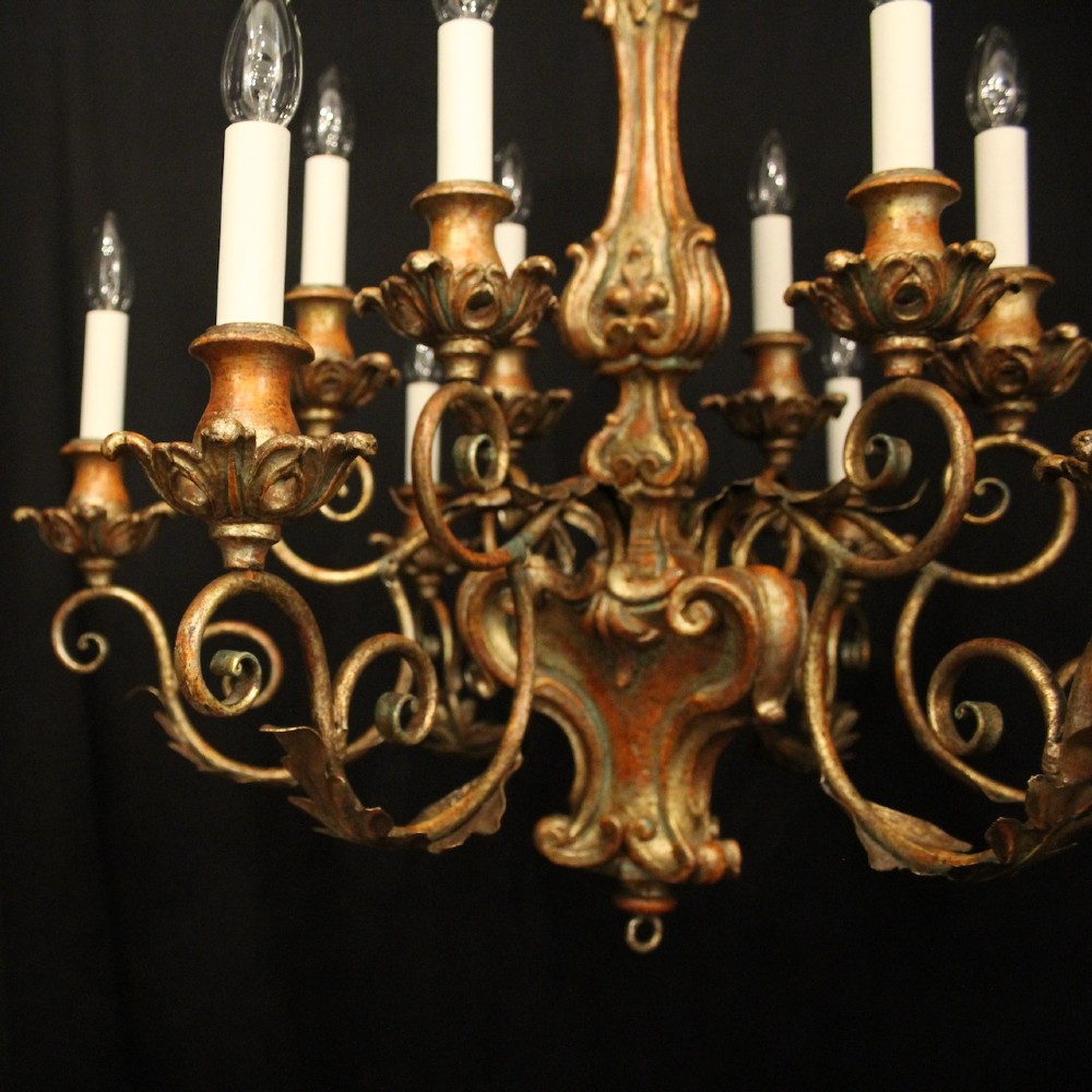 A pair of twelve-light Italian Florentine chandeliers featuring carved gilt wood scrollwork, polychrome painted details, and candle-style bulb holders. View VI