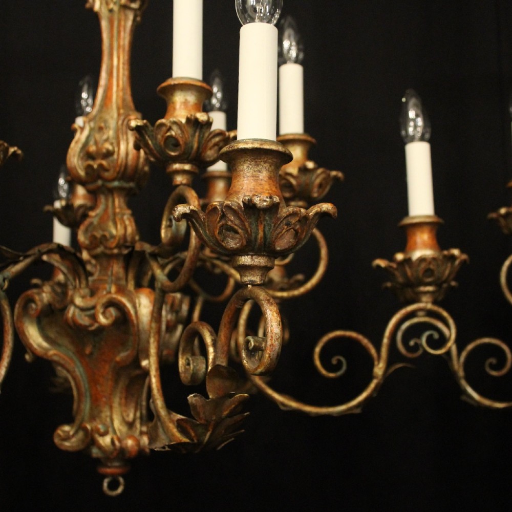 A pair of twelve-light Italian Florentine chandeliers featuring carved gilt wood scrollwork, polychrome painted details, and candle-style bulb holders. View VII