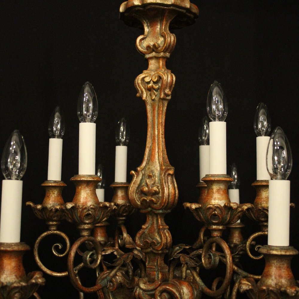 A pair of twelve-light Italian Florentine chandeliers featuring carved gilt wood scrollwork, polychrome painted details, and candle-style bulb holders. View IX
