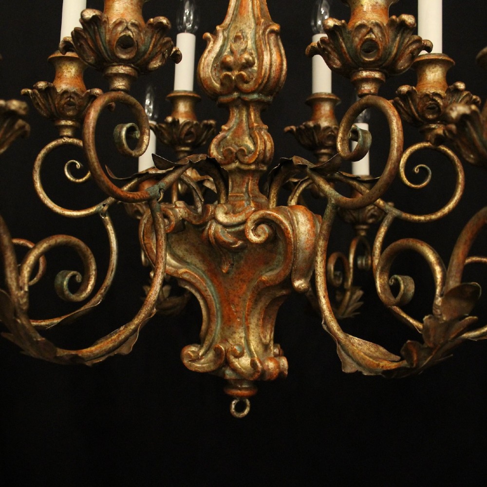 A pair of twelve-light Italian Florentine chandeliers featuring carved gilt wood scrollwork, polychrome painted details, and candle-style bulb holders. View X