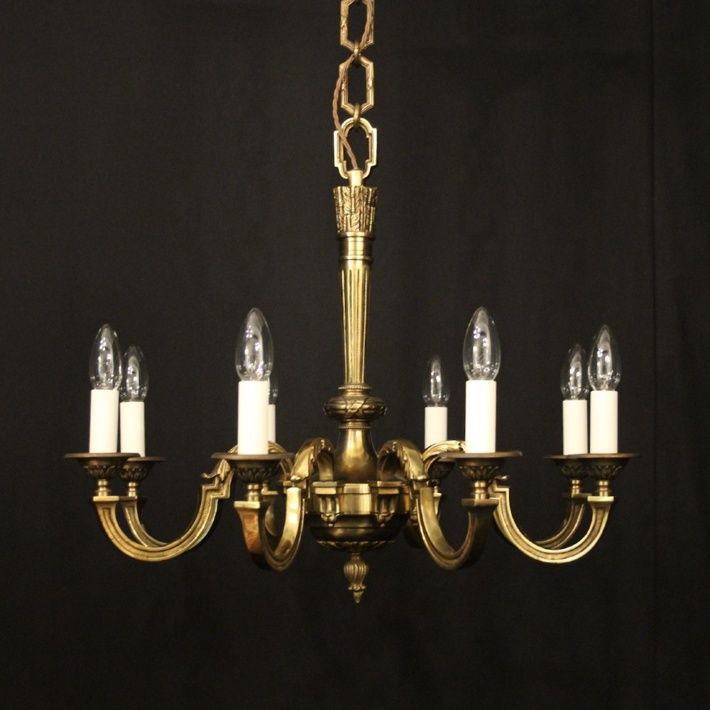 A French gilt bronze six-light chandelier featuring a central fluted stem, scrolled arms with white candle sleeves, and a geometric suspension chain.