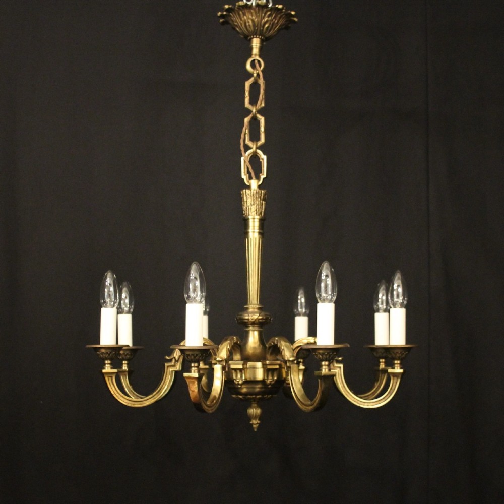 A French gilt bronze six-light chandelier featuring a central fluted stem, scrolled arms with white candle sleeves, and a geometric suspension chain. View II