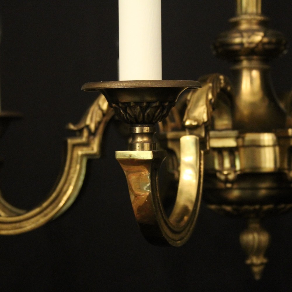 A French gilt bronze six-light chandelier featuring a central fluted stem, scrolled arms with white candle sleeves, and a geometric suspension chain. View V