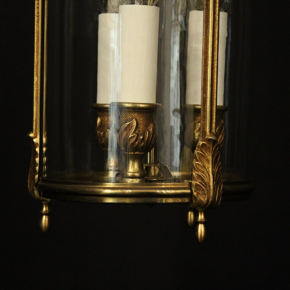 An antique French gilded bronze hall lantern featuring a cylindrical glass shade, three central candle sleeves, and ornate cast scrollwork mounts suspended from a chain. View VII