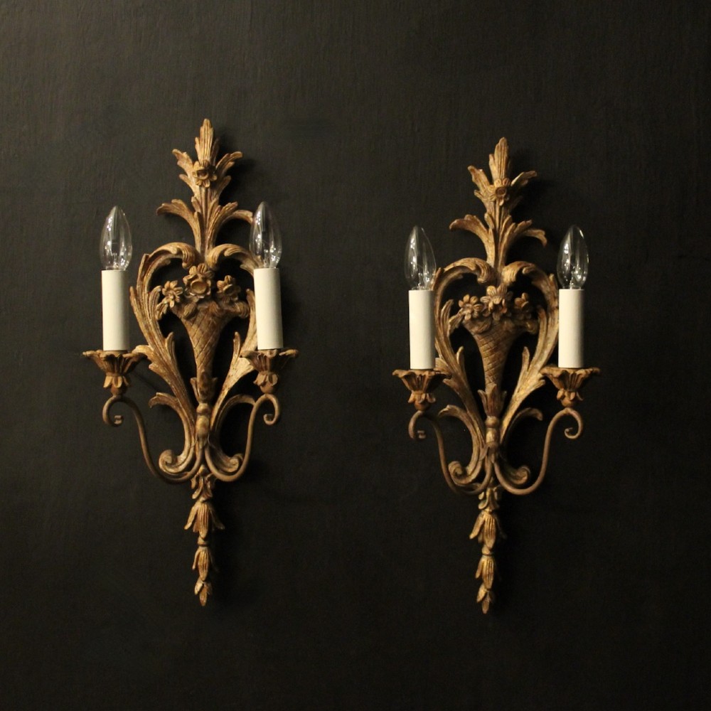 A pair of French carved wooden two-arm wall sconces featuring ornate floral basket motifs, acanthus leaf scrollwork, and white candle sleeves.