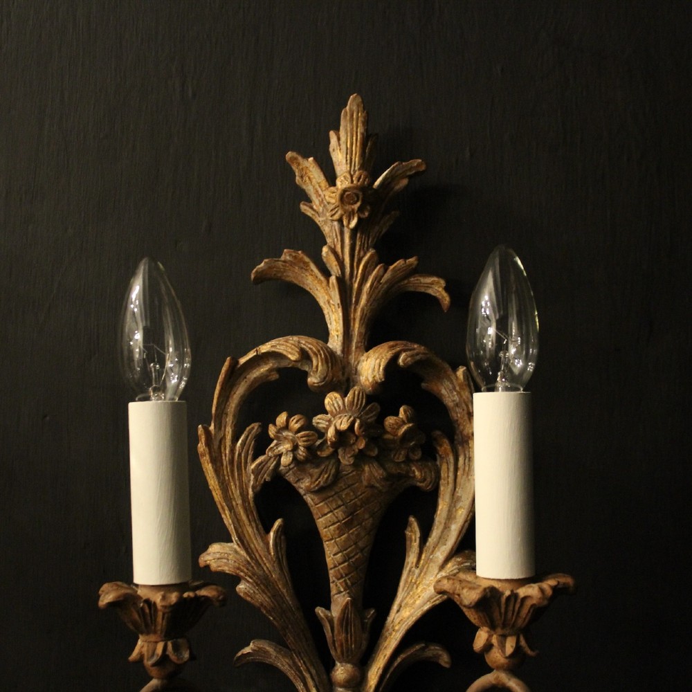 A pair of French carved wooden two-arm wall sconces featuring ornate floral basket motifs, acanthus leaf scrollwork, and white candle sleeves. View III