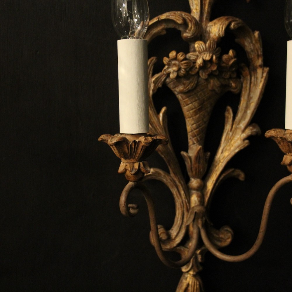 A pair of French carved wooden two-arm wall sconces featuring ornate floral basket motifs, acanthus leaf scrollwork, and white candle sleeves. View VI