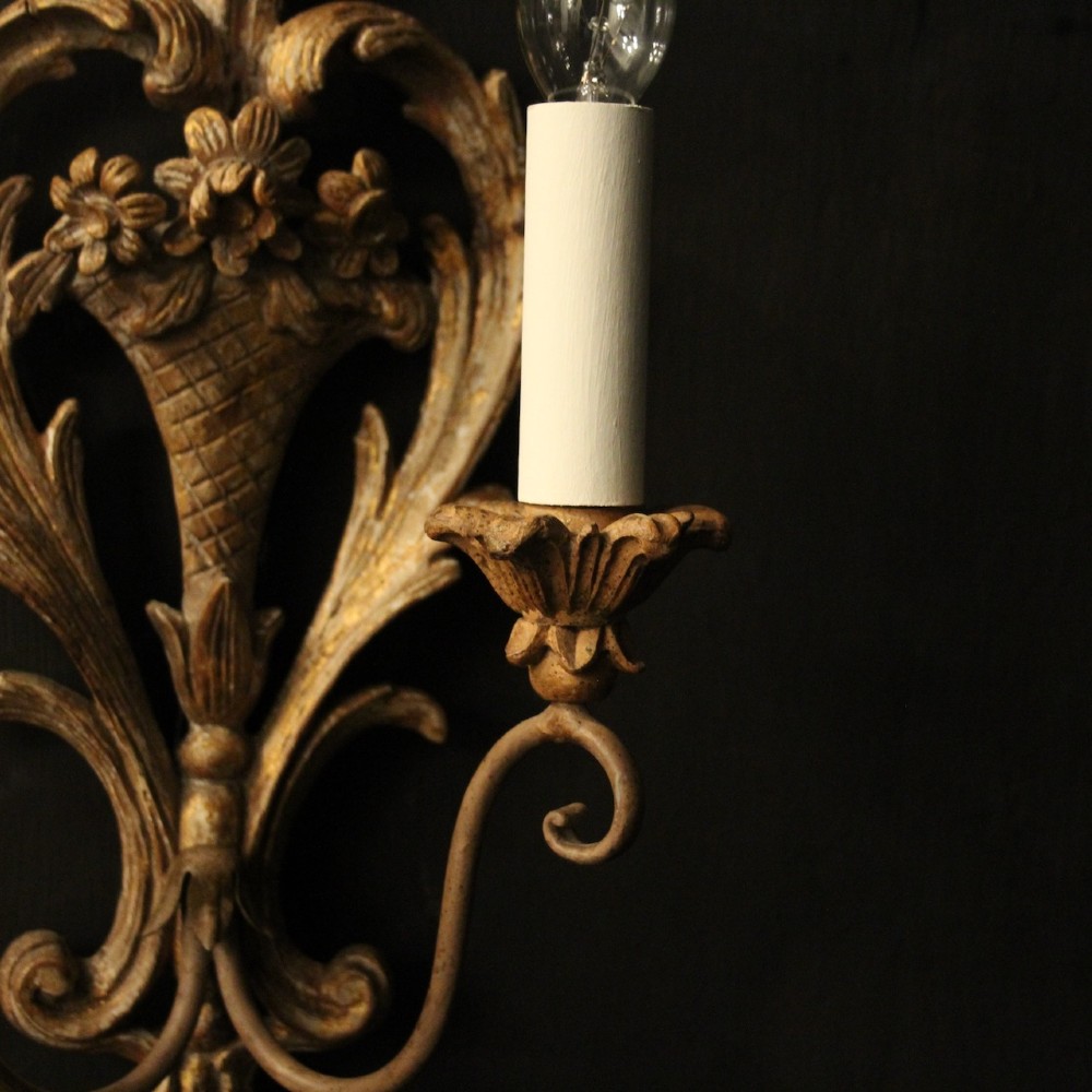 A pair of French carved wooden two-arm wall sconces featuring ornate floral basket motifs, acanthus leaf scrollwork, and white candle sleeves. View VII