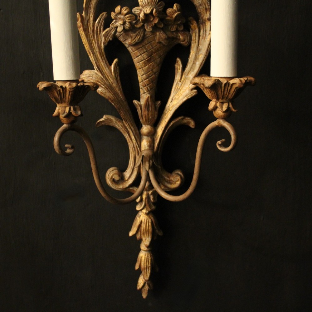 A pair of French carved wooden two-arm wall sconces featuring ornate floral basket motifs, acanthus leaf scrollwork, and white candle sleeves. View VIII
